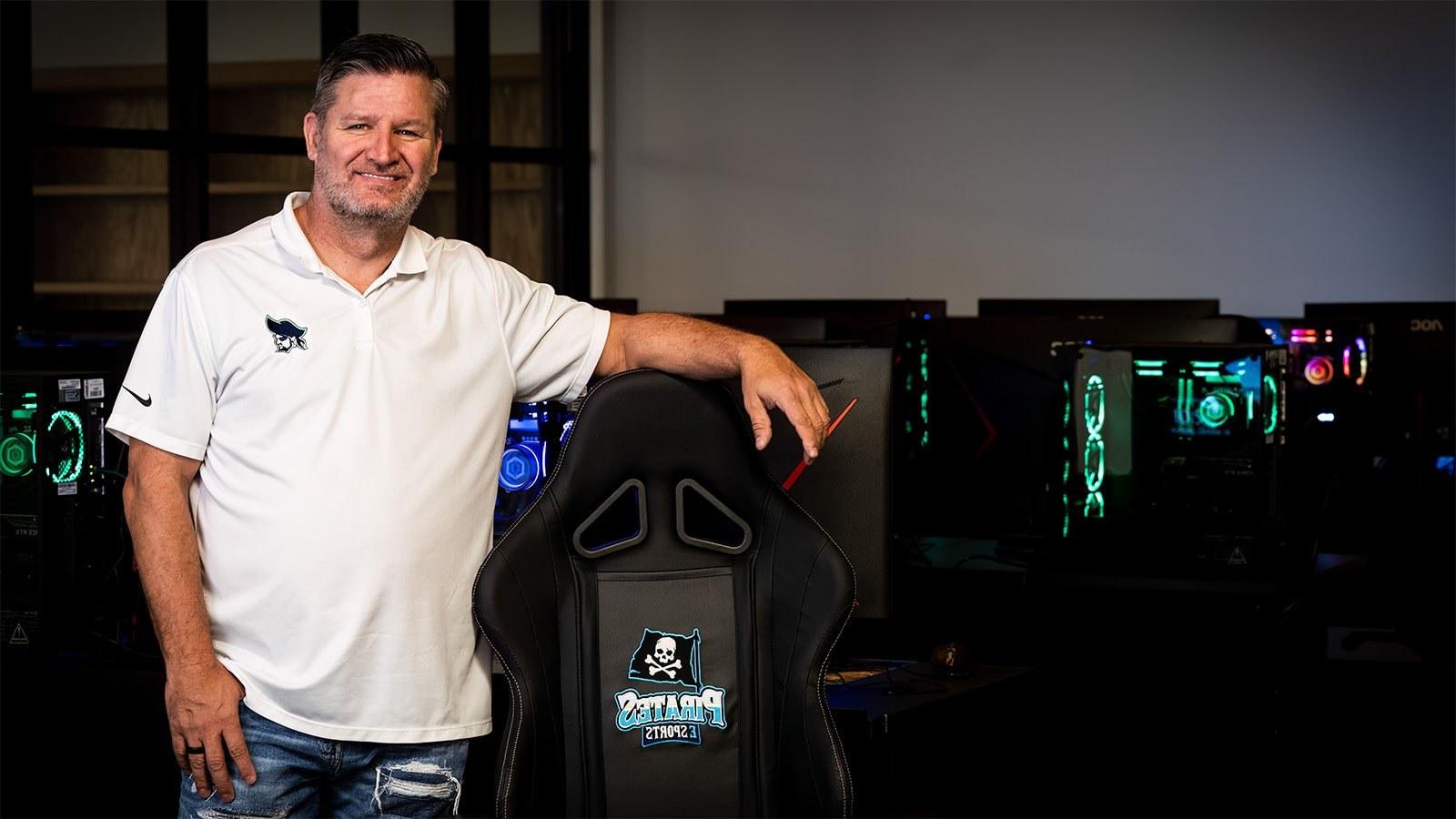 Scott Brumfield站在游戏电脑前. He is next to a PSC Pirates gaming chair 和 is wearing a Pirates shirt.